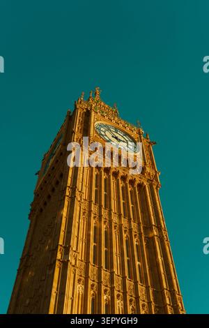 Niedrigwinkelaufnahme des berühmten Big Ben Uhrenturms in London mit einem dramatischen goldenen Leuchten vor einem leuchtenden blaugrünen Himmel. Filmisches Reisekonzept. Stockfoto