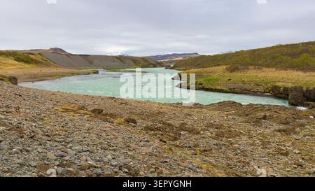 Der türkisfarbene Fluss Hvítá fließt durch eine felsige und grasbewachsene isländische Landschaft nahe Gullfoss unter einem bewölkten Himmel. Stockfoto