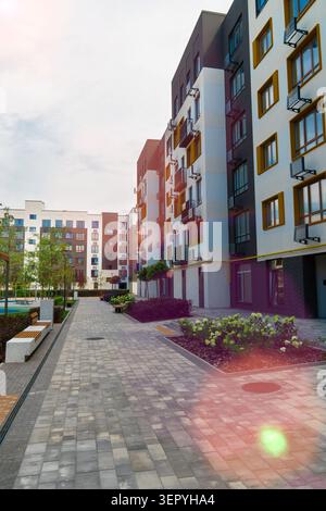 Schöner Innenhof eines modernen Wohnkomplexes mit zeitgenössischen mehrstöckigen Wohnhäusern, gepflasterten Fußwegen, Bänken und Pflanzen Stockfoto