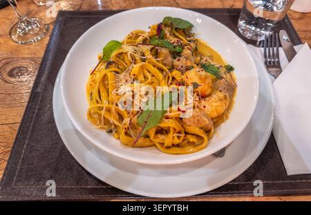 Frisch zubereitete Tagliatelle-Pasta mit Garnelen und Muscheln in cremiger Sauce, garniert mit Parmesankäse und Kräutern, verzehrfertig. Stockfoto