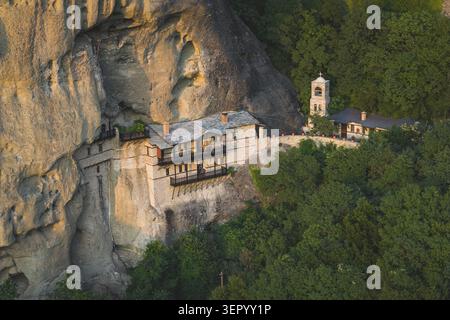 Aus der Vogelperspektive des Klosters St. Nikolaus Anapausas, erbaut in einer steilen Felsklippe, umgeben von dichtem grünen Wald in Meteora, Trikala, Griechenland. Stockfoto