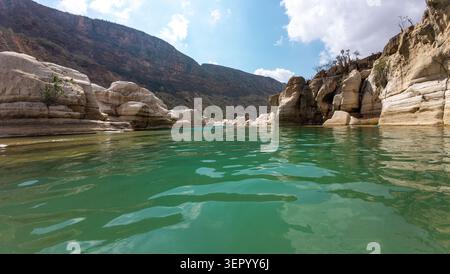Weite Aussicht auf klares türkisfarbenes Wasser, das durch einen felsigen Canyon mit weißen Steinklippen fließt, Berghänge und einen hellblauen Himmel mit Wolken. Sokotra, Stockfoto