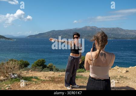 29.09.2024, Albanien, Vlora, Ksamil - Junge weibliche Touristen an der Adriaküste machen ein Erinnerungsfoto mit ihren Handys; Griechenland ist auf Th zu sehen Stockfoto