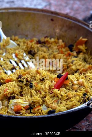 Traditionelles usbekisches Pilaw in einem großen Wok-kasan mit roter Chili-Pfeffer und Metallspachtel Stockfoto