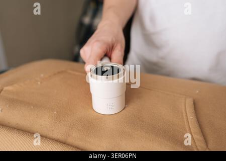 Zusammenschnitt einer Person, die einen elektrischen Stoffrasierer verwendet, um Pilling und Fusseln von einem Sweatshirt zu entfernen und das Aussehen der Kleidung sowie die Textilqualität zu erhalten Stockfoto