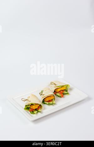 Ein minimalistischer Hochwinkel aus drei goldenen, zarten Wraps mit frischem Gemüse, serviert auf einem eleganten weißen Teller Stockfoto