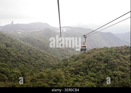 Blick aus einem hohen Winkel auf die Ngong Ping 360 Seilbahnhütten, die sich über die üppigen grünen Berge auf Lantau Island in Hongkong bewegen Stockfoto