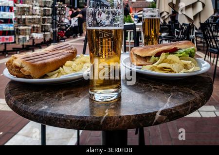 Zwei Pints Birra Korca und zwei Panini-Sandwiches serviert mit Kartoffelchips auf einem Marmortisch in einem Café im Freien in Tirana, Albanien. Stockfoto