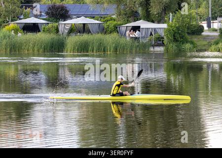 Bila Tserkva, Ukraine, 2026.06.16: Ein männlicher Athlet mit einer Kappe und gelber Sportbekleidung paddelt mit einem langen gelben Rennkajak oder Kanu auf einem ruhigen Fluss sur Stockfoto