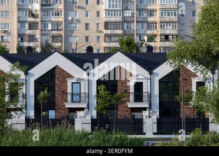 Eine horizontale architektonische Aufnahme, die einen starken Kontrast zwischen einer neu gebauten Reihe moderner Stadthäuser mit weißen und Ziegelfassaden und einer großen, Stockfoto