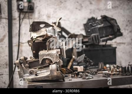 Auf einem Metalltisch in einer schwach beleuchteten Garage stapelt sich eine Sammlung von ausrangierten Automobilteilen und Metallfragmenten Stockfoto