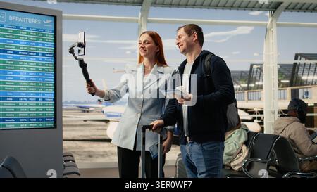Mann und Frau Influencer erstellen Reisevlog am Flughafen, halten Telefon und nehmen Video auf, während sie sich auf den Abflug vorbereiten. Präsenz in sozialen Medien, die ihre Online-Reise dokumentieren. Stockfoto