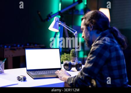 Männlicher Freelancer mit einem digitalen Laptop mit leerem weißen Bildschirm. Junger Mann, der vor seinem tragbaren Computer sitzt und eine isolierte Mockup-Chroma-Schlüsselvorlage zeigt. Stockfoto