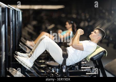 Junger Mann, der eine Glute-Brückenmaschine während des Trainings im Fitnessstudio benutzt Stockfoto