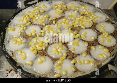 Khanom krok Thai Kokospankuchen mit gelbem Mais in einer traditionellen gusseisernen Pfanne auf einem Street Food Markt in Thailand. Stockfoto
