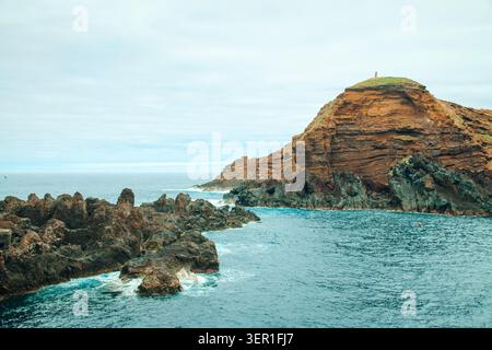 Eine wunderschöne Küstenlandschaft, die die einzigartigen vulkanischen Basalt-Felsformationen und das zerklüftete Riff in Porto Moniz, Madeira, Portugal, erfasst. Das pulsierende turq Stockfoto
