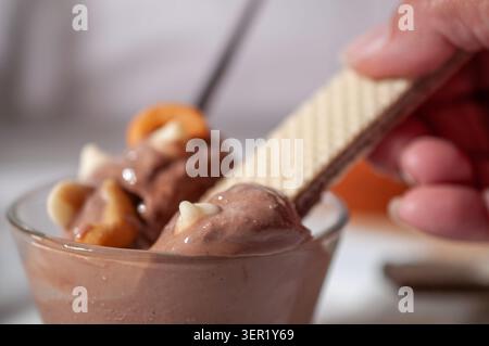 Schokoladeneis in einer Glasschale, mit Cashewnüssen und weißen Schokoladenchips oben, beleuchtet durch Sommersonnenlicht von einem Fenster, mit einem weißen Stockfoto