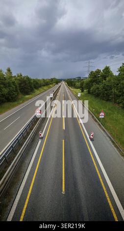 Geradeaus erstreckt sich eine leere Autobahn mit Baustellenschildern, umgeben von Bäumen, unter bewölktem Himmel mit Straßenschildern, Oberpfalz Stockfoto