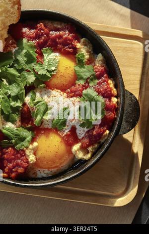 Shakshuka, ein Gericht aus dem Nahen Osten und nordafrika, mit Eiern in einer würzigen Tomatensauce, garniert mit frischen Kräutern Stockfoto