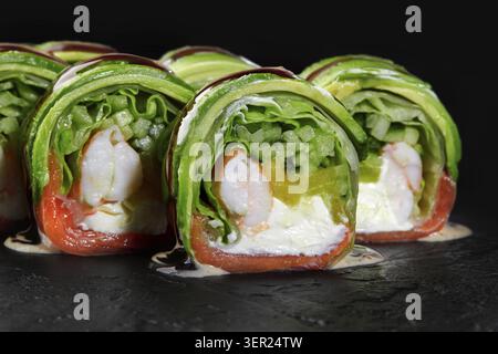 Köstliche Frühlingsbrötchen gefüllt mit Garnelen, Lachs, Avocado, Gurke, Salat und Frischkäse, bedeckt mit Sauce auf schwarzem Hintergrund Stockfoto