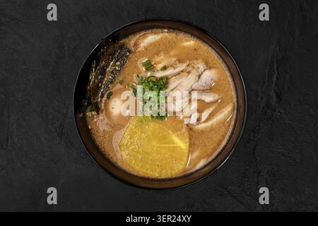 Hühnerramen mit Ei, Nori-Algen, Menma und gehackten grünen Zwiebeln serviert in einer schwarzen Schüssel auf dunklem Hintergrund Stockfoto
