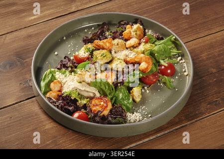 Köstlicher caesar-Salat mit gegrillten Garnelen, Salat, Croutons, Kirschtomaten und Parmesan, serviert auf einem Teller auf einem Holztisch Stockfoto