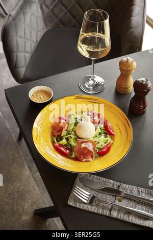 Köstliche Gourmet-Pasta mit Burrata, Schinken und Pesto-Sauce serviert auf gelbem Teller mit Weißwein Stockfoto