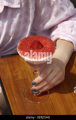 Frau genießt ein schickes Dessert in einem Glas mit cremiger Basis, gefriergetrockneten Erdbeeren und einem Hauch von rotem Samtpulver Stockfoto