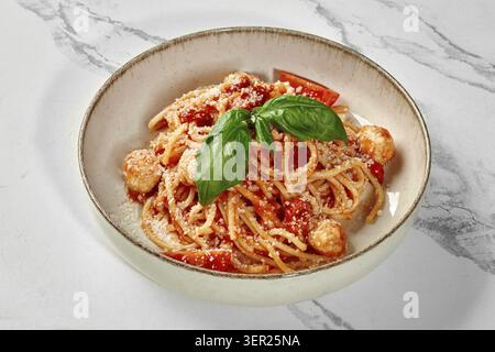 Spaghetti mit Tomatensauce, Fleischbällchen, Tomaten und Basilikum, serviert in einer Schüssel auf einem Marmortisch Stockfoto