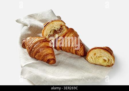 Frisch gebackene Croissants, eines in Scheiben geschnitten, mit einer reichhaltigen Schokoladenfüllung, präsentiert auf einer einfachen Leinenserviette Stockfoto