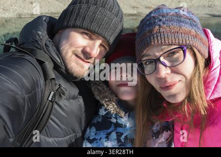 Familienselfie auf der Winterreise. Mutter, Vater und Sohn machen Selfie-Fotos im Wald am schönen, sonnigen Wintertag in den Altai-Bergen. Reiseurlaub Stockfoto