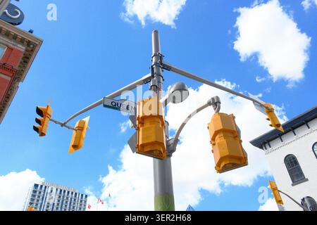 Mehrere Ampeln und ein Schild auf der Queen Street an einer Kreuzung, die sich vor einem blauen Himmel mit Wolken befindet, Kitchener, Ontario, Kanada. Stockfoto
