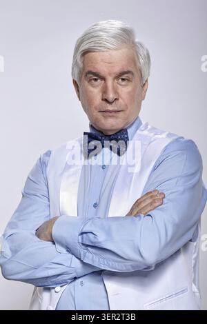 Studio Portrait von älteren Mann mit einem ernsten Gesichtsausdruck auf grauem Hintergrund. Reifer Mann im blauen Hemd mit Weste und Fliege. Ein Blick auf die Kamera Stockfoto