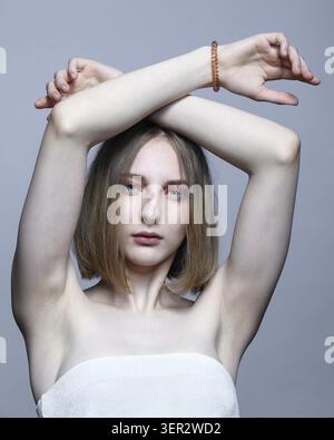 Nahporträt der schönen jungen blonden Frau. Eine Frau mit erhobenen Händen schaut in die Kamera Stockfoto