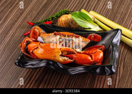 Frisch gedämpfte Krabben, serviert mit Zitronengras, Galgant, Kaffir-Limettenblättern und roten Chilis auf einem dunklen Teller mit leuchtender Orangenschale und Aroma Stockfoto
