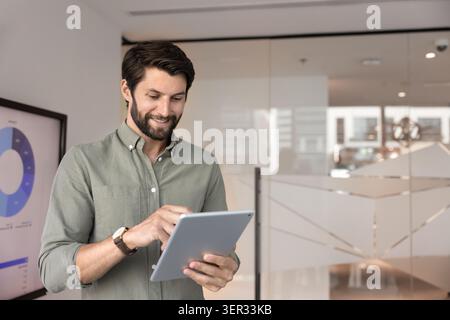 Lächelnder Geschäftsmann, der im Firmenbüro am Tablet arbeitet Stockfoto