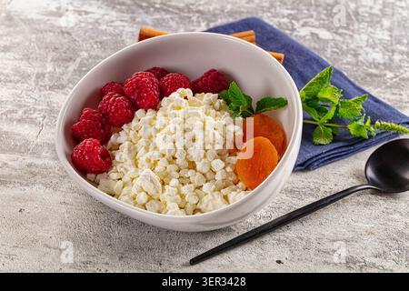 Gesunde Frühstücksschale mit Hüttenkäse, leuchtenden roten Himbeeren, getrockneten Orangen-Aprikosen, frischen grünen Minzblättern Stockfoto