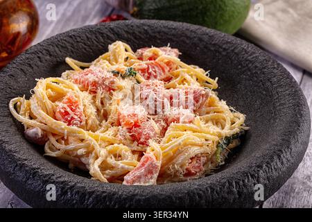 Köstliches cremiges Pastagericht mit Lachsstücken, Spinat und geriebenem Käse, serviert in einer rustikalen Schüssel aus schwarzem Stein. Perfekt zum Fotografieren von Speisen und Stockfoto