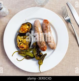 Schweinefleischwürste mit gegrilltem Gemüse auf einer Keramikplatte Stockfoto