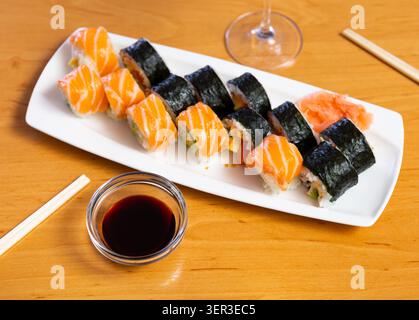 Verschiedene Arten von Maki, Uramaki, mit Lachs, serviert mit einer Schüssel Sojasauce auf Teller im Restaurant Stockfoto