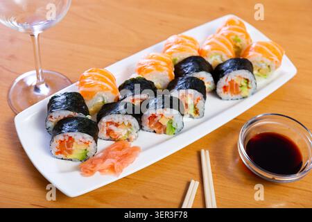 Verschiedene Arten von Maki, Uramaki, mit Lachs, serviert mit einer Schüssel Sojasauce auf Teller im Restaurant Stockfoto