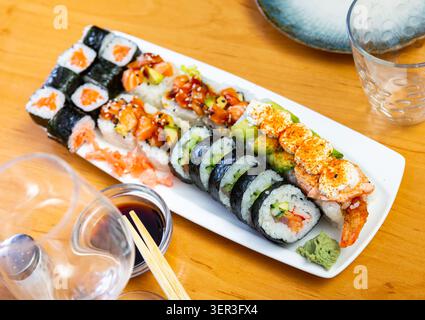 Verschiedene Arten von Maki, Uramaki, mit Lachs, serviert mit einer Schüssel Sojasauce auf Teller im Restaurant Stockfoto