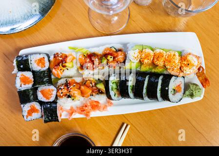 Verschiedene Arten von Maki, Uramaki, mit Lachs, serviert mit einer Schüssel Sojasauce auf Teller im Restaurant Stockfoto