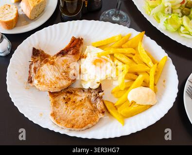 Gebratenes Schweinefleisch mit Kartoffeln und Spiegeleiern auf Teller Stockfoto