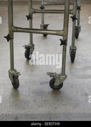 Nahaufnahme eines Gerätewagens aus Metall mit Rohrbeinen, Quertraversen und Lenkrollen mit Montagehalterungen, die auf einem abgenutzten Betonboden stehen Stockfoto