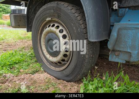 Nahaufnahme eines plattplatzierten Reifens eines gewerblichen Transportwagens, der auf unbefestigtem Boden und grünem Gras auf einer Baustelle geparkt ist. Entlüftete Räder und Stockfoto