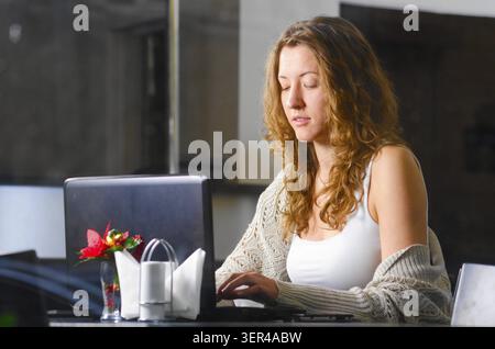 Die junge Frau sitzt im Café und arbeitet am Laptop. Blick durch die Fensterscheibe von außen Stockfoto