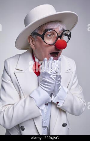 Überraschter Clown mit Handschuhen in der Nähe seines Gesichtes. Ein älterer Clown mit weißem Mantel und Hut Stockfoto