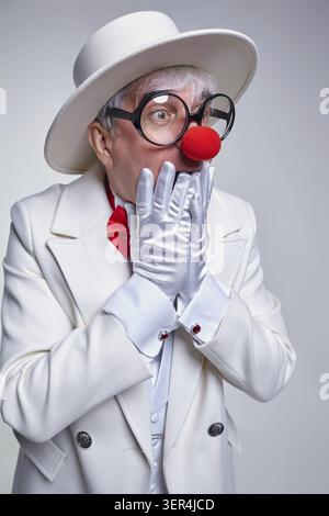 Überraschter Clown mit Handschuhen in der Nähe seines Gesichtes. Ein älterer Clown mit weißem Mantel und Hut Stockfoto