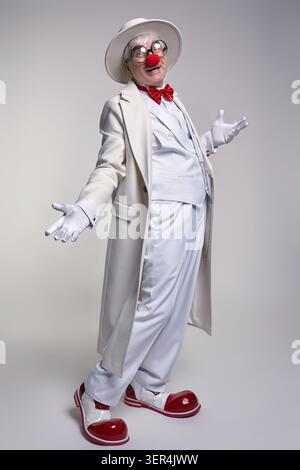 Ein älterer Clown mit weißem Mantel und Hut. Der Mann trägt große rote Clownstiefel aus Lackleder Stockfoto